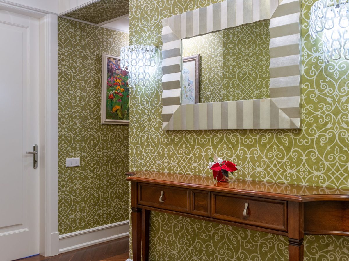 Entry hall with an olive-green damask wallpaper, a wooden console table and a striped-frame mirror