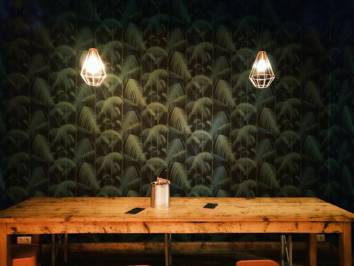 Dining table beneath two pendant lamps against a dark green palm-leaf wallpaper