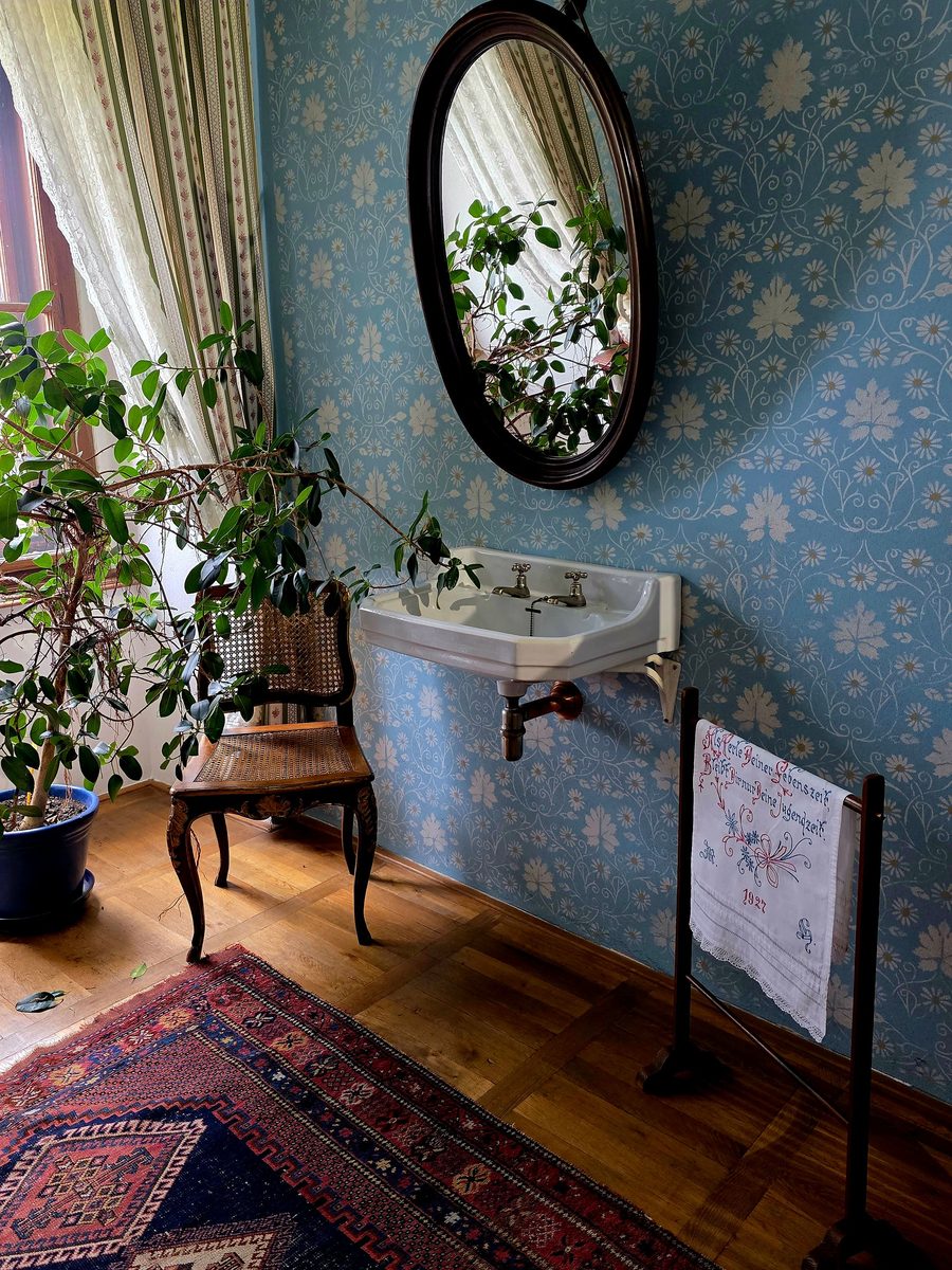 Powder room with a blue floral wallpaper, a round black mirror, a wall-mounted sink and potted plants