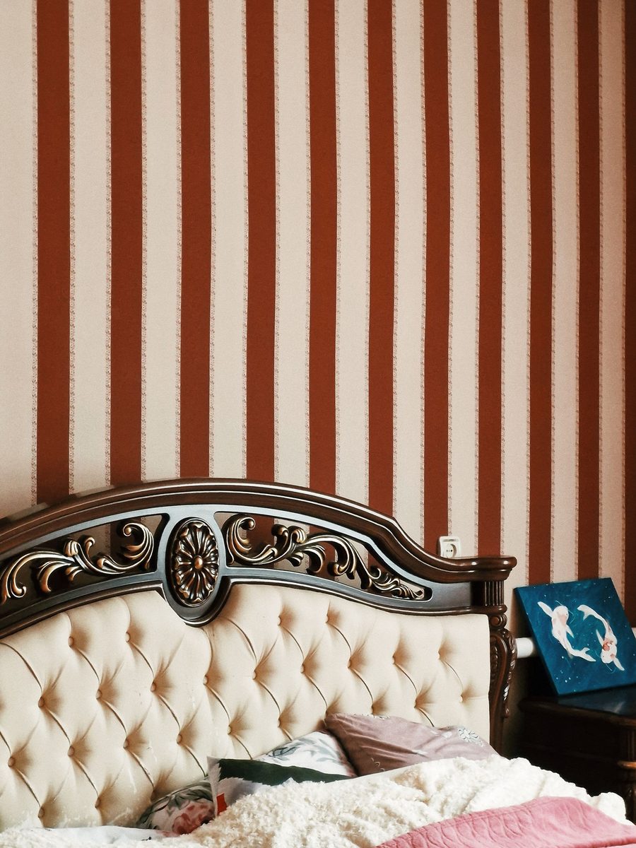 Bedroom with a terracotta and cream striped wallpaper above a tufted, carved wooden headboard