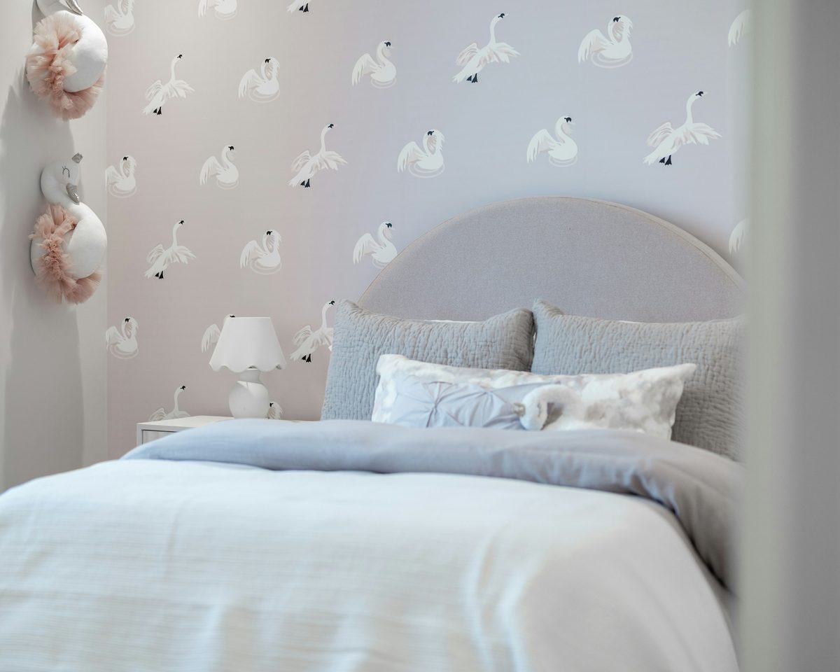 Soft grey bedroom with a delicate swan-patterned wallpaper behind an upholstered arched headboard
