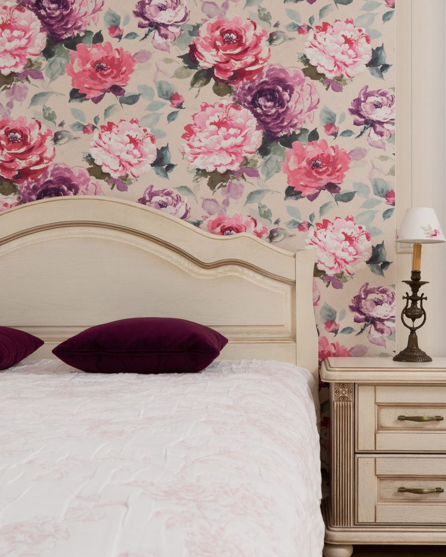 Bedroom accent wall in a large-scale pink and plum peony wallpaper behind a cream carved headboard