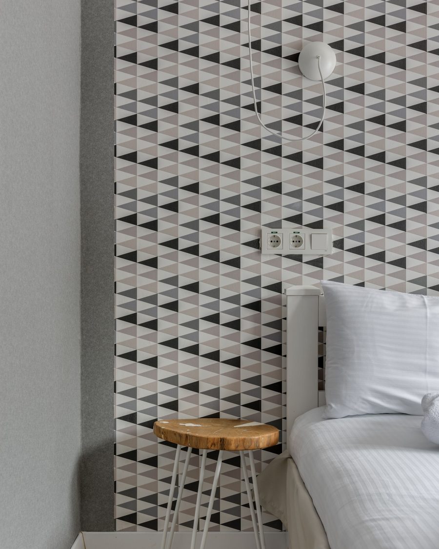 Corner where a grey and white triangle-patterned wallpaper meets a plain painted wall beside a wooden stool