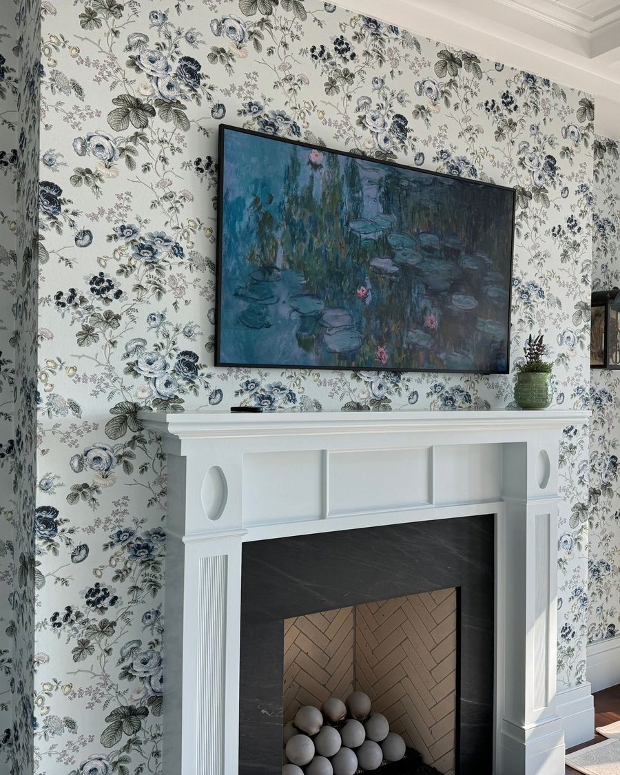 Living room fireplace wall covered in a blue and white floral wallpaper with a white mantel and crown molding